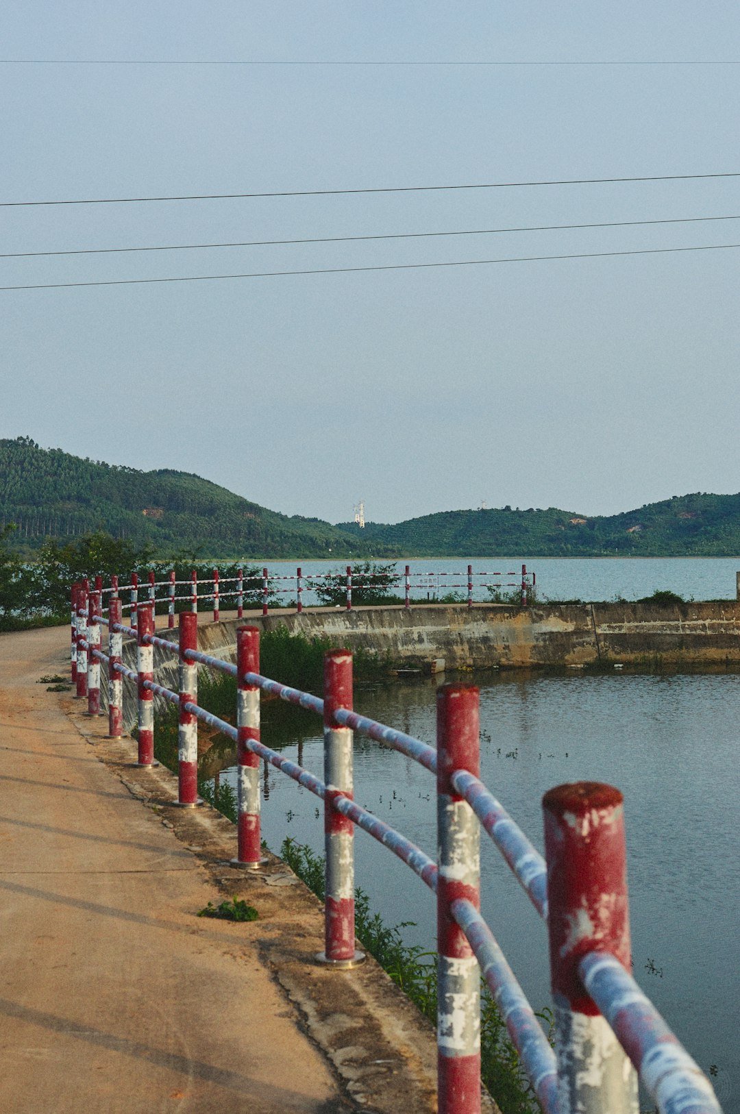 a-red-fence-with-white-poles-and-a-body-of-water-in-the-background-decnnkr8baw